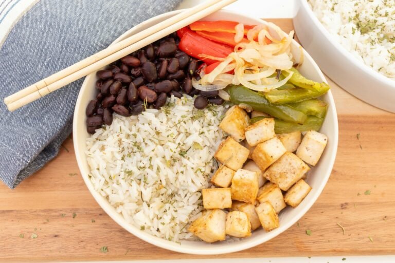 Delicious vegan rice bowl with tofu, black beans, and vegetables on a wooden table.
