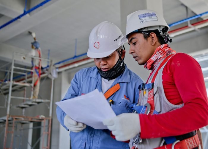 Two engineers in safety helmets reviewing construction plans at a worksite.